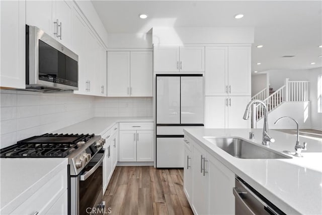kitchen with white cabinets, stainless steel appliances, light countertops, and a sink