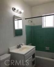 full bathroom featuring tiled shower / bath, vanity, toilet, and a wealth of natural light