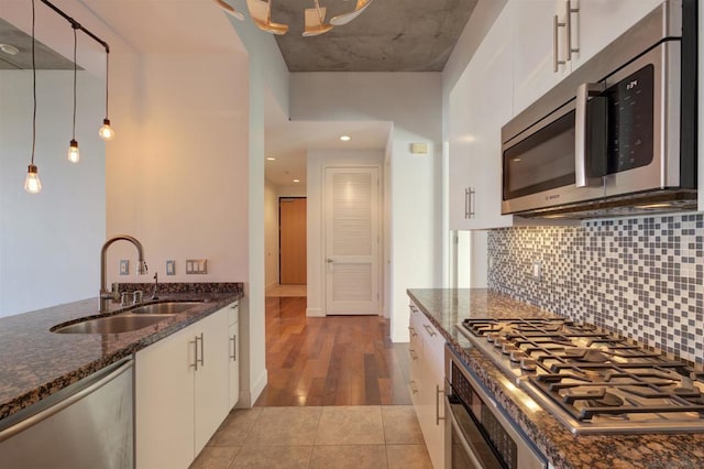 kitchen with white cabinets, appliances with stainless steel finishes, decorative light fixtures, dark stone counters, and sink