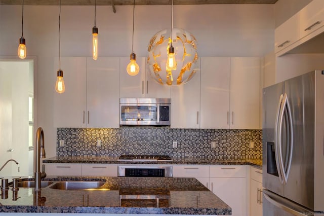 kitchen with tasteful backsplash, pendant lighting, stainless steel appliances, white cabinets, and dark stone counters