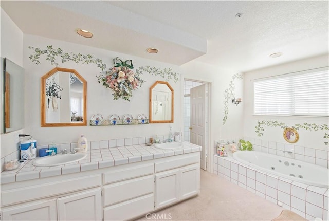 bathroom featuring a textured ceiling, vanity, and a relaxing tiled tub