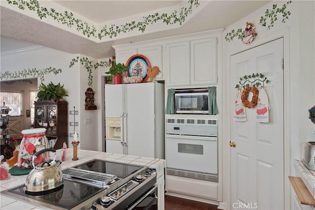 kitchen with white cabinetry, stainless steel appliances, a raised ceiling, dark hardwood / wood-style floors, and tile countertops