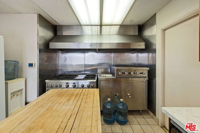 kitchen with wall chimney range hood, stainless steel stove, light tile patterned floors, and dark brown cabinets