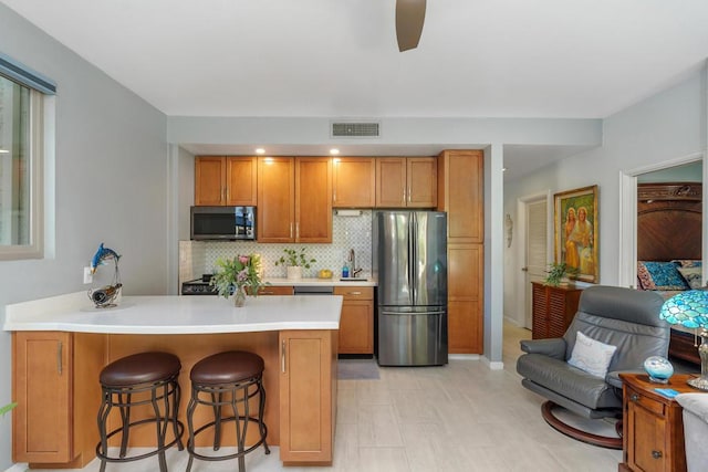 kitchen featuring tasteful backsplash, kitchen peninsula, a kitchen bar, sink, and appliances with stainless steel finishes