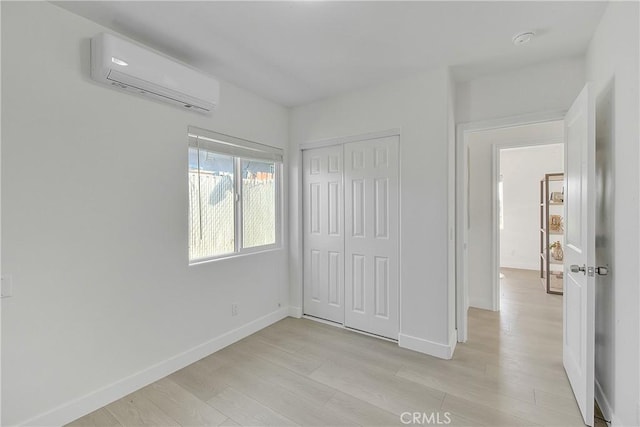 unfurnished bedroom with an AC wall unit, light hardwood / wood-style flooring, and a closet