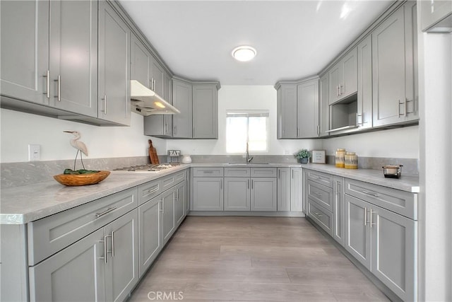 kitchen featuring light stone counters, light hardwood / wood-style floors, stainless steel gas cooktop, sink, and gray cabinets