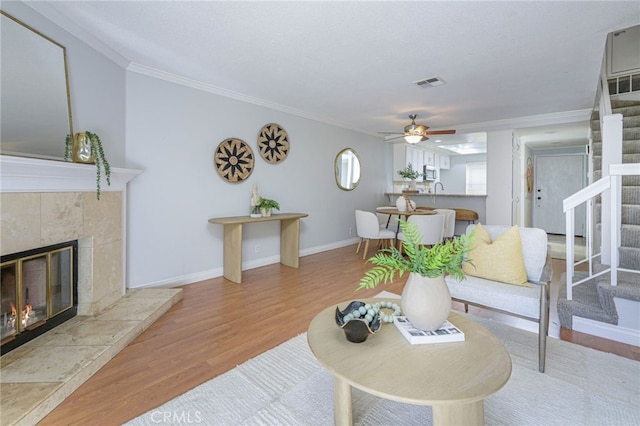 living room with light hardwood / wood-style floors, ceiling fan, a textured ceiling, crown molding, and a tile fireplace