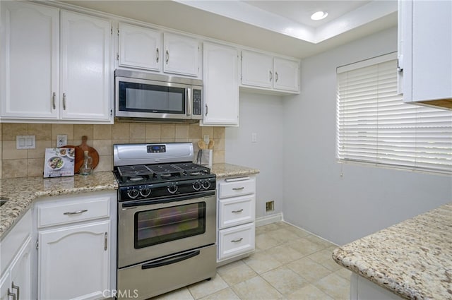 kitchen with backsplash, light tile patterned floors, appliances with stainless steel finishes, white cabinets, and light stone counters