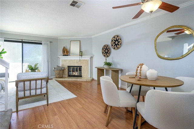 dining space with light hardwood / wood-style floors, a tile fireplace, and crown molding