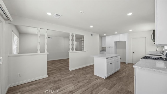 kitchen with hardwood / wood-style floors, light stone counters, a center island, and white cabinets