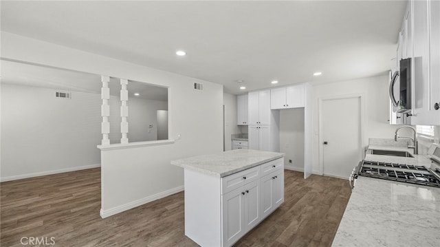 kitchen with dark hardwood / wood-style floors, a kitchen island, light stone counters, and white cabinetry