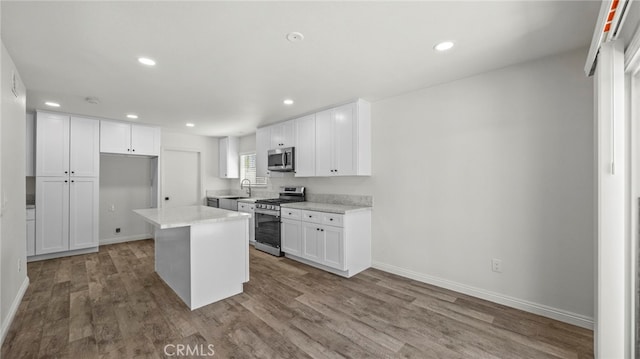 kitchen with light stone counters, stainless steel appliances, hardwood / wood-style flooring, a center island, and white cabinetry