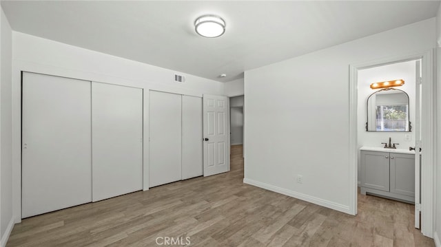 unfurnished bedroom featuring ensuite bathroom, two closets, sink, and light hardwood / wood-style floors