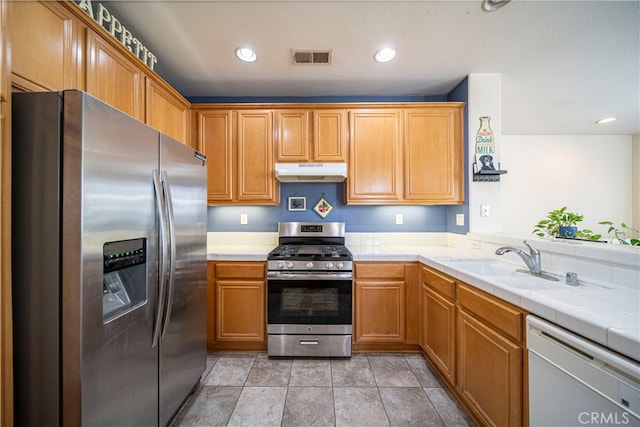 kitchen with sink, stainless steel appliances, tile counters, and kitchen peninsula