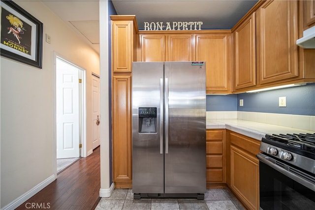 kitchen with black gas stove, light hardwood / wood-style flooring, stainless steel fridge with ice dispenser, ventilation hood, and tile counters