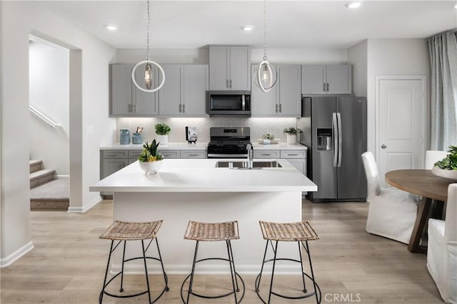 kitchen with gray cabinetry, light hardwood / wood-style floors, an island with sink, and appliances with stainless steel finishes