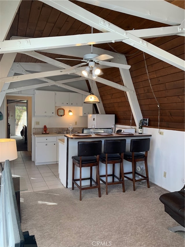 kitchen with ceiling fan, white cabinetry, lofted ceiling with beams, light carpet, and a breakfast bar area