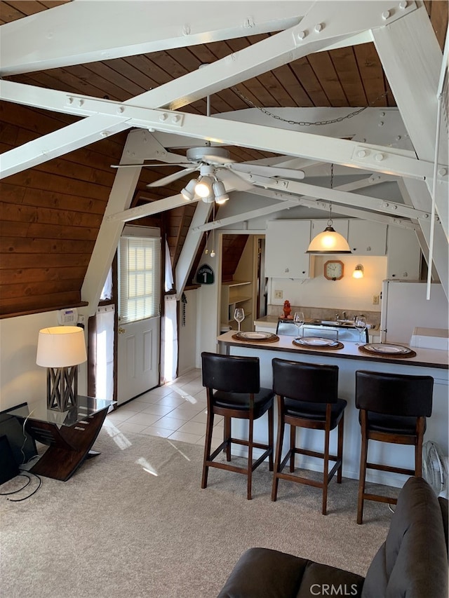 kitchen with ceiling fan, vaulted ceiling with beams, wood ceiling, hanging light fixtures, and light colored carpet