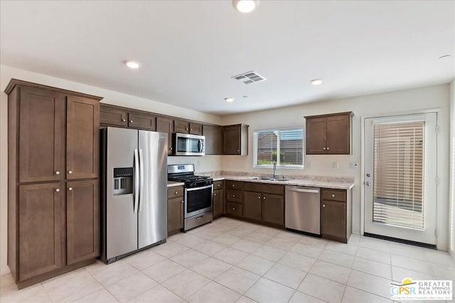 kitchen with dark brown cabinets, light tile patterned floors, stainless steel appliances, and sink