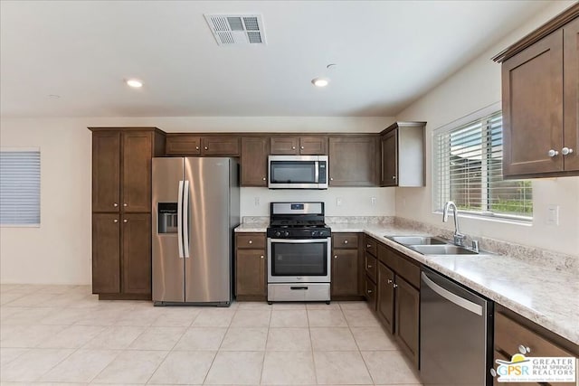 kitchen with light tile patterned floors, appliances with stainless steel finishes, sink, and dark brown cabinetry