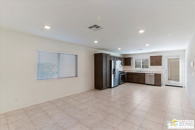 kitchen featuring dark brown cabinetry, light tile patterned floors, stainless steel appliances, and sink