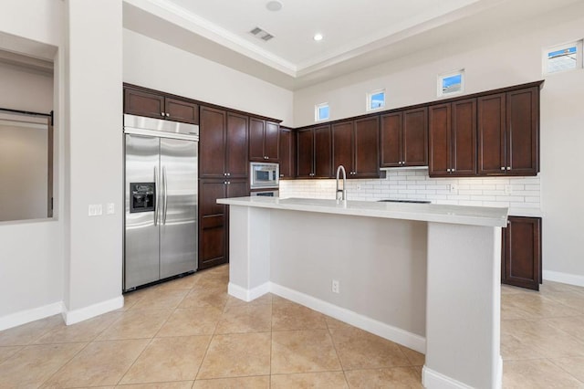 kitchen with built in appliances, decorative backsplash, dark brown cabinetry, and a center island with sink