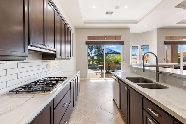 kitchen with a raised ceiling, sink, light stone counters, and stainless steel appliances