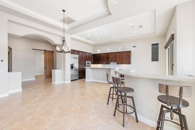 kitchen with a breakfast bar area, built in appliances, a raised ceiling, pendant lighting, and a barn door