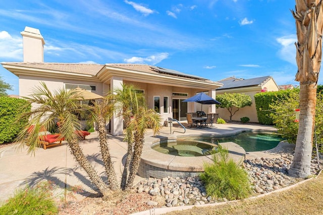 rear view of property with a swimming pool with hot tub, a patio area, and solar panels