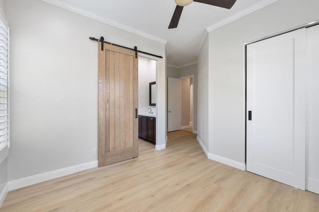 unfurnished bedroom featuring light wood-type flooring, ornamental molding, a closet, ceiling fan, and a barn door