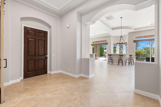 tiled foyer entrance with crown molding and a notable chandelier