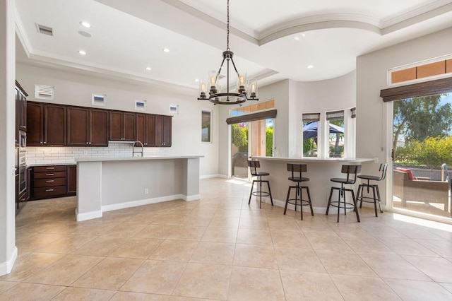 kitchen featuring tasteful backsplash, decorative light fixtures, a raised ceiling, and a center island with sink