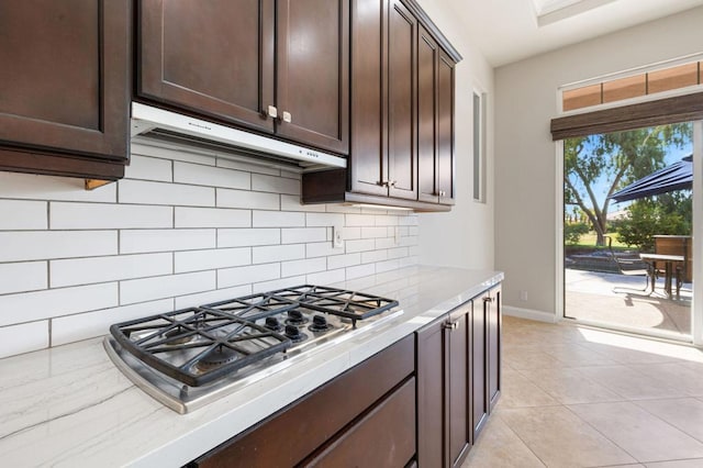 kitchen featuring stainless steel gas stovetop, light tile patterned flooring, dark brown cabinets, and decorative backsplash