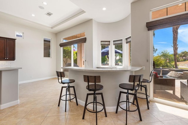 kitchen featuring decorative backsplash, light tile patterned flooring, a raised ceiling, and a kitchen bar