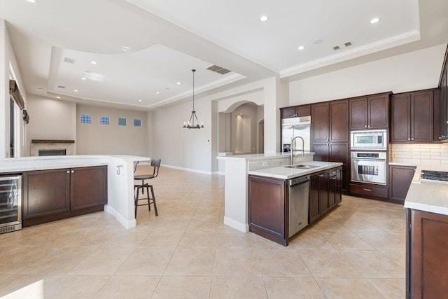 kitchen featuring an island with sink, sink, built in appliances, and a tray ceiling