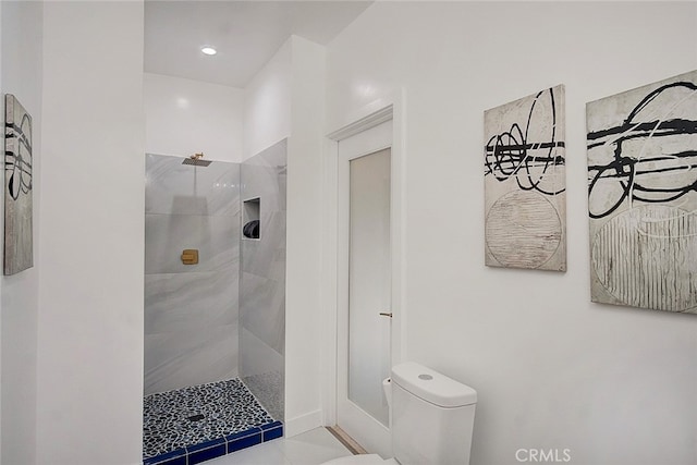 bathroom with tile patterned floors, a tile shower, and toilet