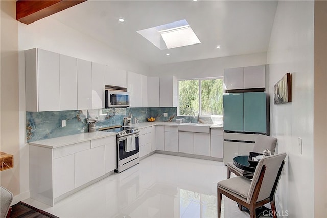 kitchen with sink, backsplash, white cabinetry, stainless steel appliances, and lofted ceiling with skylight