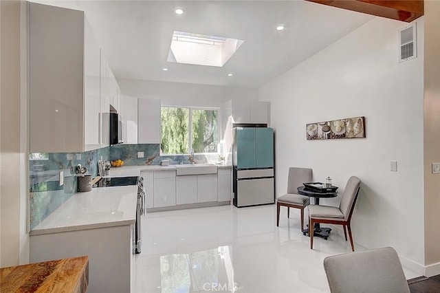 kitchen with white cabinets, sink, stainless steel appliances, lofted ceiling with skylight, and decorative backsplash