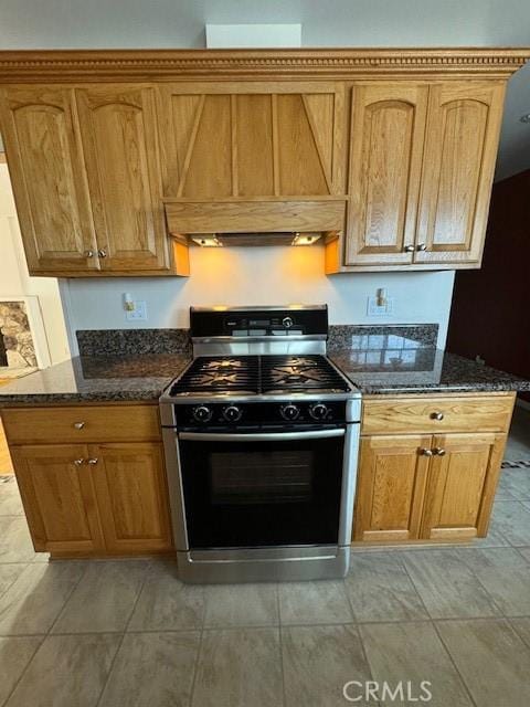 kitchen with light tile patterned flooring, stainless steel gas range oven, dark stone counters, and custom exhaust hood