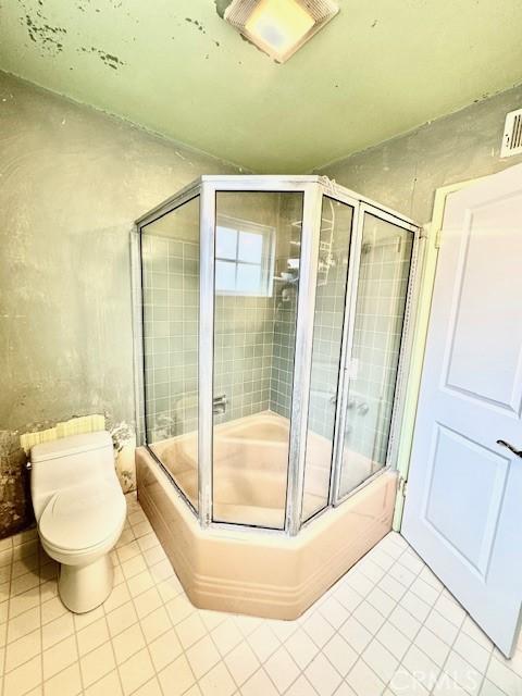 bathroom with tile patterned flooring, toilet, and shower / bath combination with glass door