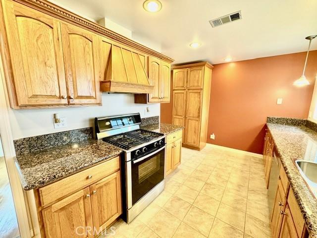 kitchen with custom exhaust hood, dark stone countertops, decorative light fixtures, and gas range