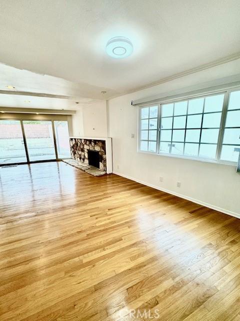 unfurnished living room with light wood-type flooring, a stone fireplace, a wealth of natural light, and ornamental molding