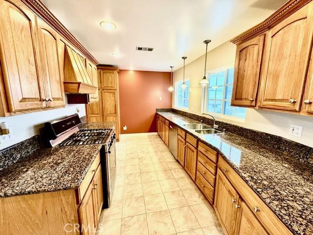 kitchen with sink, dark stone countertops, pendant lighting, appliances with stainless steel finishes, and custom exhaust hood