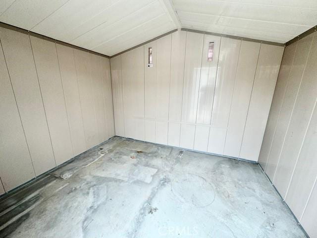 empty room featuring lofted ceiling and wooden walls