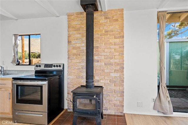 kitchen with dark tile patterned flooring, stainless steel electric range, sink, a wood stove, and light brown cabinetry