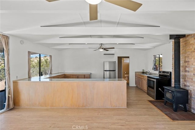 kitchen with a wood stove, light brown cabinets, stainless steel appliances, and lofted ceiling with beams