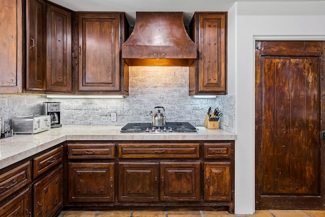 kitchen with dark brown cabinets, premium range hood, stainless steel gas cooktop, and tasteful backsplash