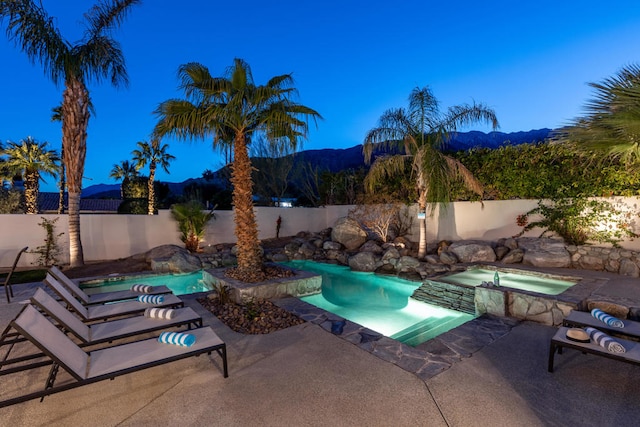 pool at dusk featuring an in ground hot tub, a patio, and a mountain view