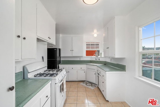 kitchen featuring sink, white cabinetry, light tile patterned floors, black refrigerator, and white gas range oven