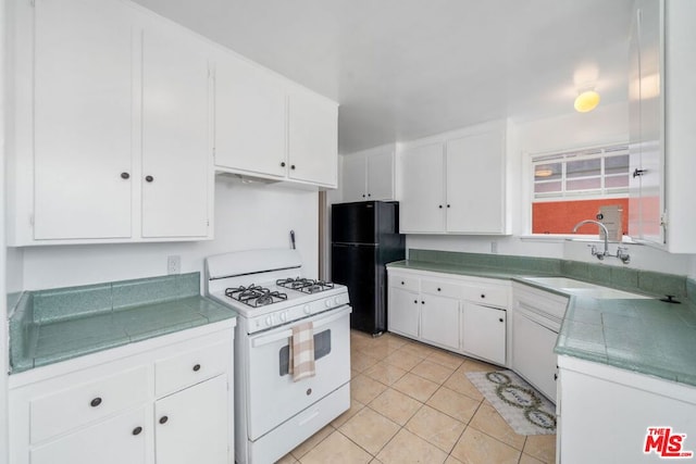 kitchen featuring black refrigerator, light tile patterned floors, white gas range oven, and white cabinets